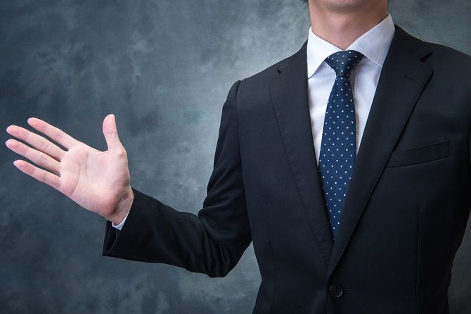 片方の手のひらをこちらに向けて立つビジネスマン