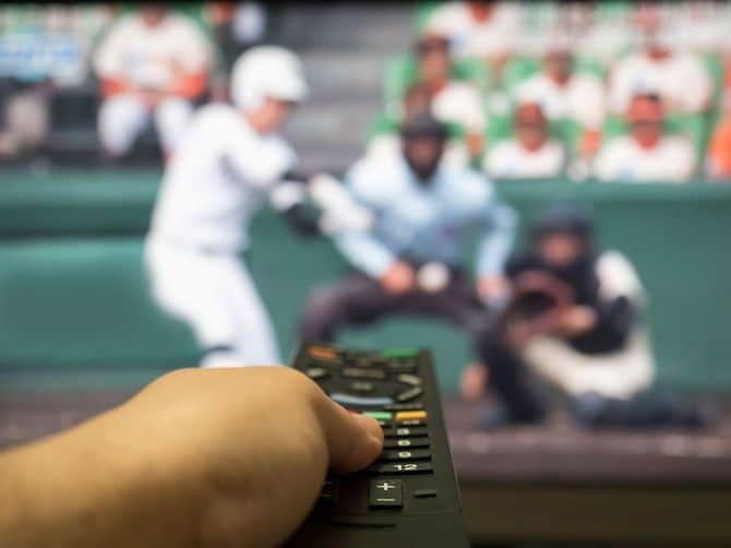 野球の試合が映るテレビ画面と、リモコンを操作する人の手