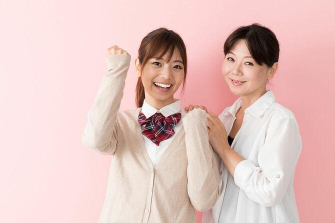 制服を着てガッツポーズをとる娘とその肩に手を乗せる母