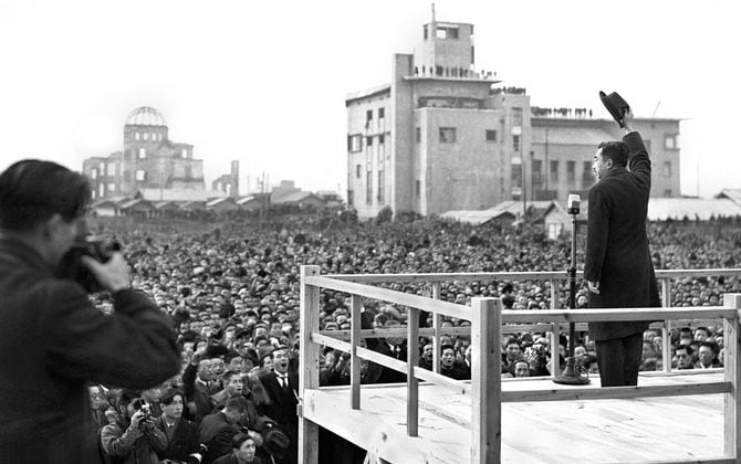 1947年12月7日、広島市を訪問し集まった人びとに帽子を振って応える昭和天皇。向かって左手奥に原爆ドームが見える
