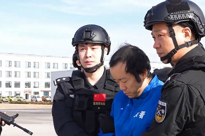 2026年1月8日に中国公安部が公開した日付不詳の映像から切り出されたこの画像は、北京で、詐欺組織の首謀者とされるチェン・ジー（Chen Zhi、中央）が、警備員に付き添われて中国南方航空の機内から降りる様子