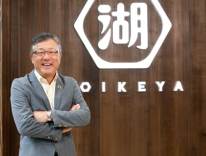 新生・湖池屋の企業ロゴの前に立つ佐藤章社長。