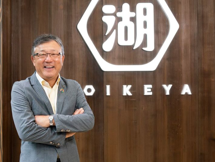 新生・湖池屋の企業ロゴの前に立つ佐藤章社長。