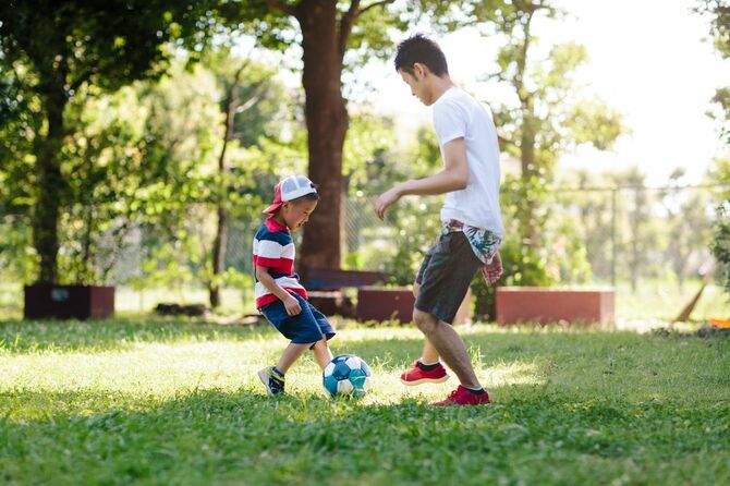 朝の公園で子供とサッカーをする父親