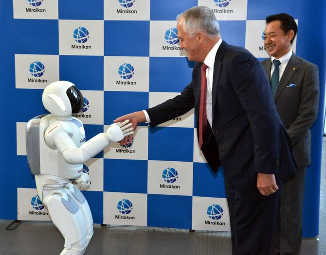 2015年12月18日、東京の日本科学未来館で、博物館長で元宇宙飛行士の毛利衛氏（右）が見守る中、日本の自動車大手ホンダ自動車の人型ロボット「アシモ」と握手するオーストラリアのマルコム・ターンブル首相（肩書はいずれも当時）