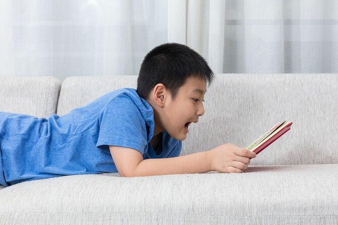 小さな男の子がソファで本を読む
