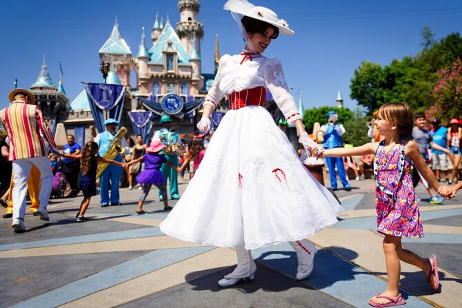 カリフォルニア州アナハイムにあるディズニーランドにて、メアリー・ポピンズがシンデレラの城の前で歌とダンスを踊る子供たちの列をリードしている