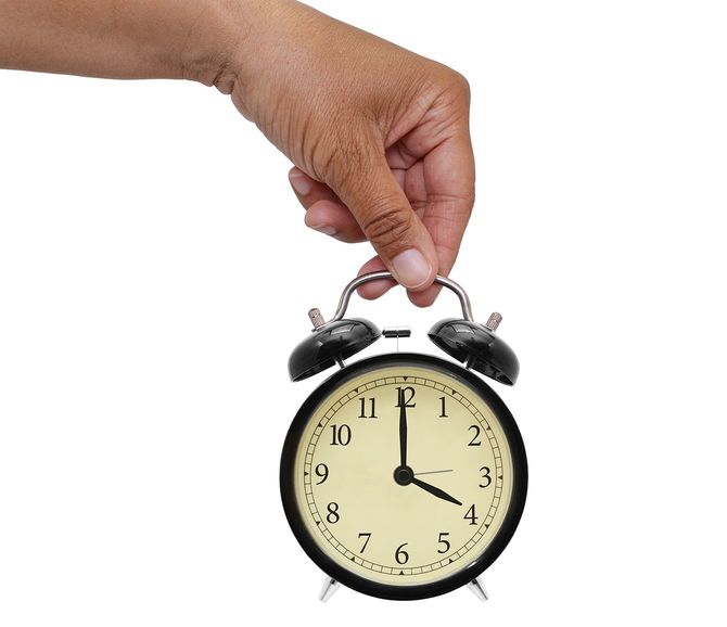 白い背景に分離された4時の目覚まし時計を握る手