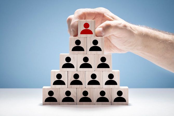 木製ブロックピラミッドの頂上にいる赤く塗られたブロックに触れている手