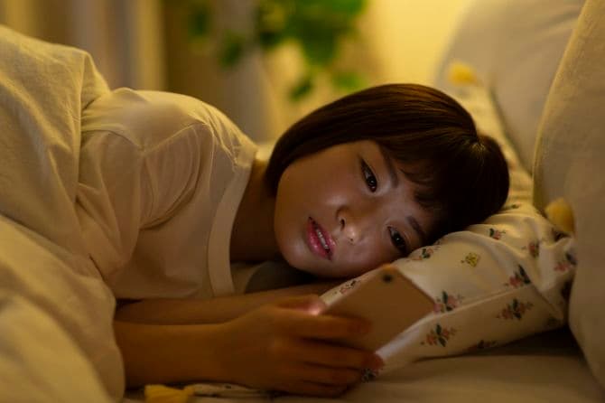 ベッドでスマホを見る若い女性