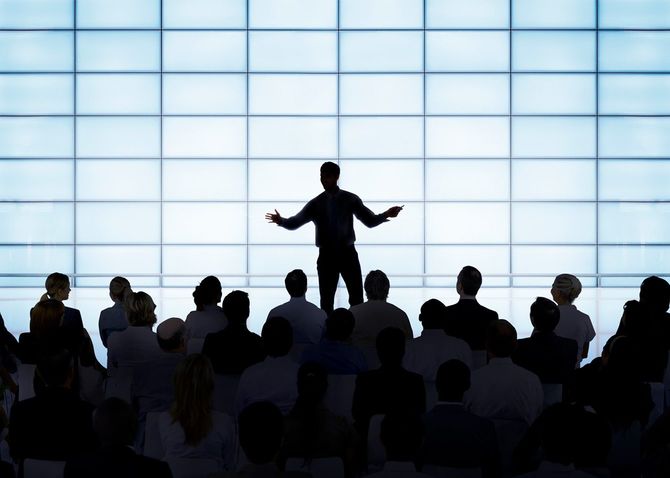 舞台上でジェスチャーを交えて話す人