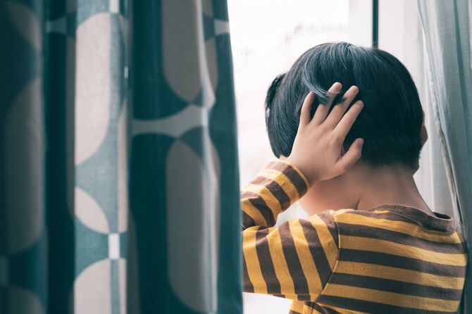 耳をふさいで、窓の近くで立っている男の子
