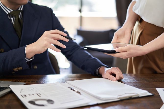 タブレットを持つ部下に、書類を広げて説明する上司