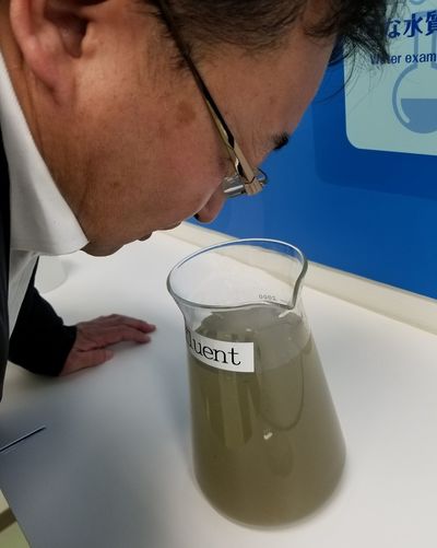 下水処理場に到着したばかりの下水を嗅ぐ筆者（神舘）