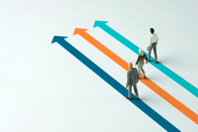 矢印の先に向かって歩く3人のビジネスパーソンの人形