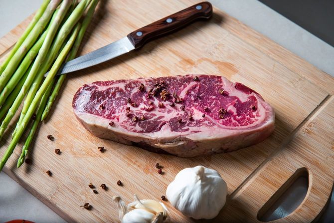 まな板の上にコショウをまぶしたステーキ肉、アスパラ、ニンニク