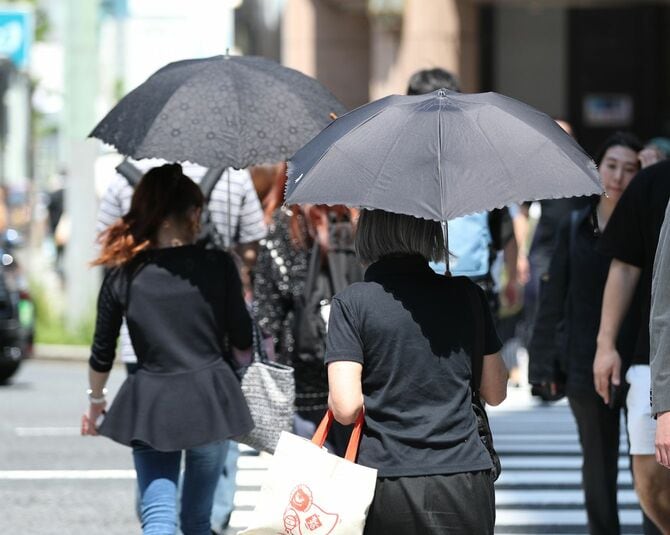 強い日差しの中、傘を差して歩く人たち＝2024年4月25日午後、東京都中央区