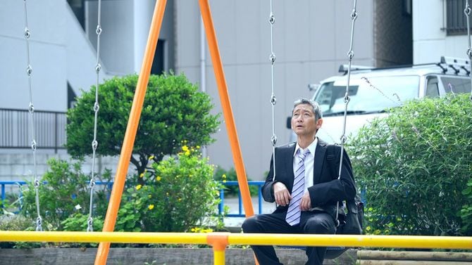 ブランコに座って遠くを見つめる中年のビジネスマン