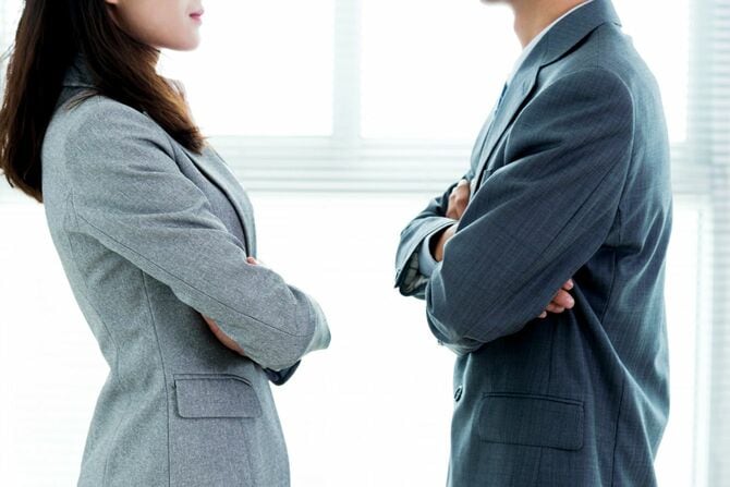 腕を組んで向かい合う二人のビジネスパーソン