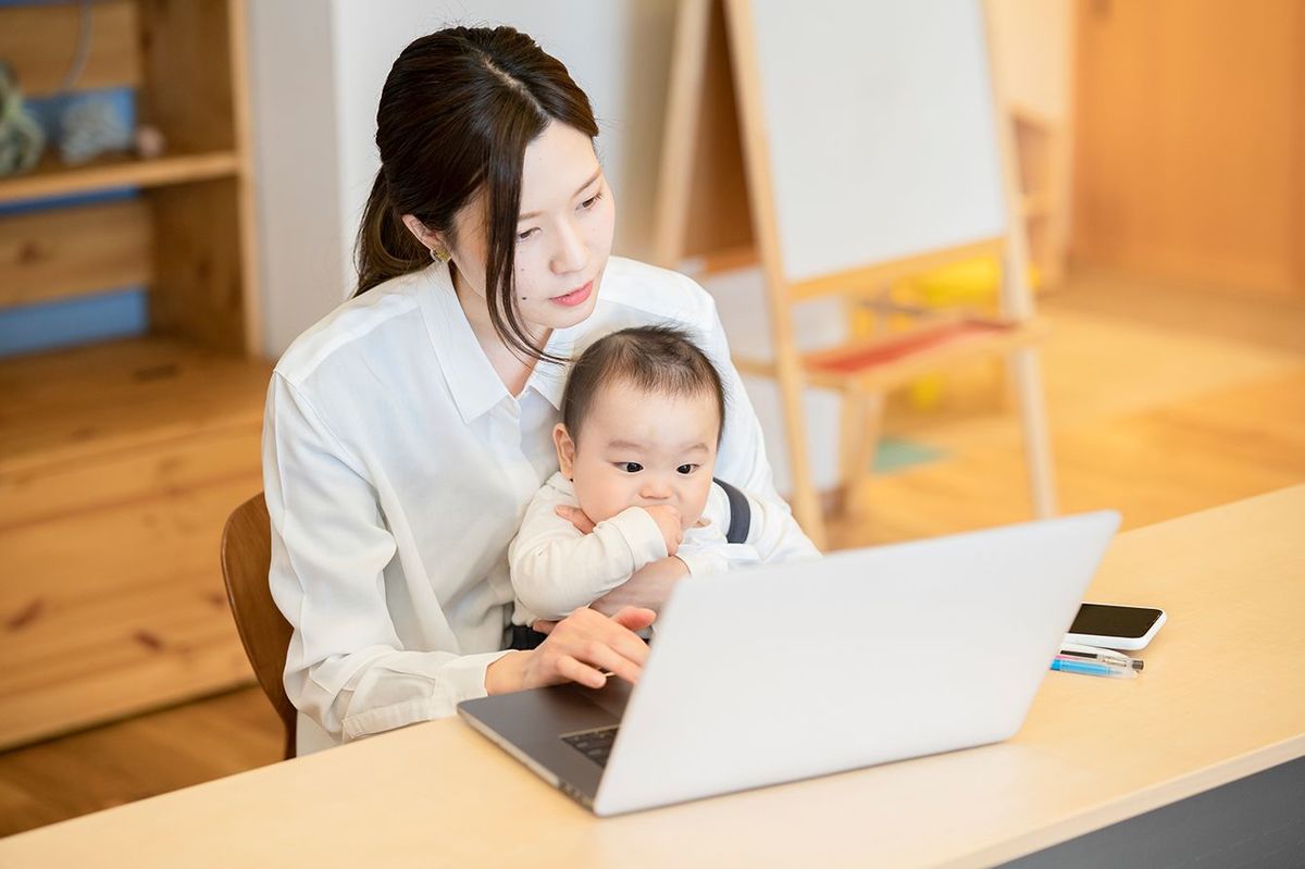 赤ちゃんを抱き、屋内でラップトップを操作するアジアの女性