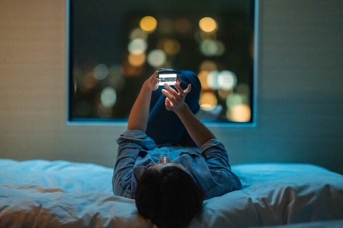 ベッドに横たわり、夜にスマートフォンを使用する女性