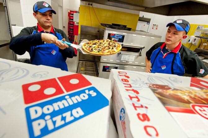 2010年11月4日、ドイツ・ベルリンにあるアメリカのピザチェーンのドミノ・ピザのドイツ1号店で、顧客にピザを手渡すスタッフ。ドミノ・ピザは、11月6日にオープンする1号店で、ドイツ市場への参入を目標としている。