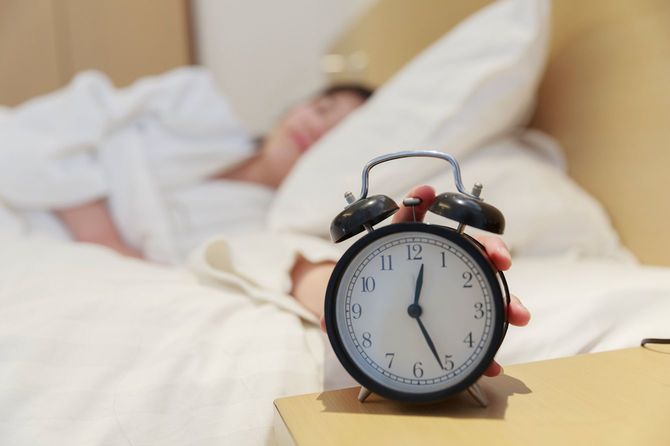 ベッドの中で時計に手を伸ばす女性