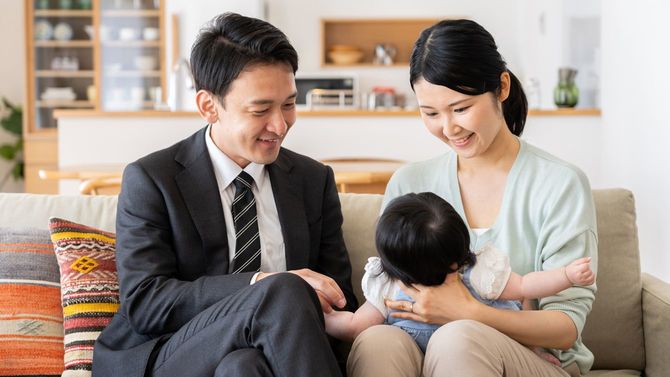 リビングで赤ちゃんにほほ笑みかける若い夫婦