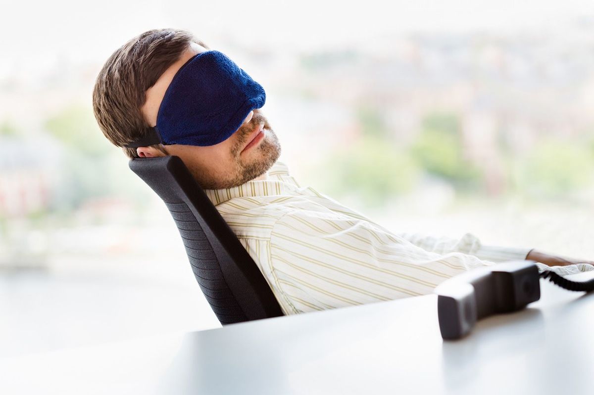 アイマスクをしてオフィスの椅子で仮眠を取る人