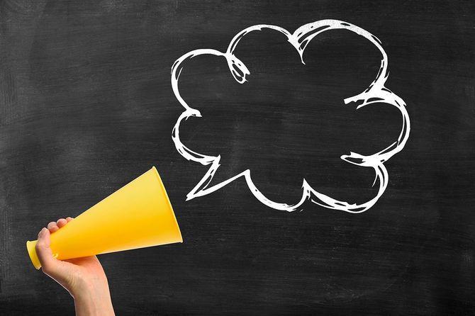 黒板に空白の吹き出しを持つメガホンを持つ手