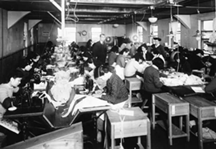 室町本社工場での作業風景。右の立っている女性が渡辺あさ野〔昭和27年（1952）頃〕（出典＝『<a href="https://www.amazon.co.jp/exec/obidos/ASIN/4833425025/presidentjp-22" target="_blank">ブラジャーで天下をとった男 ワコール創業者 塚本幸一</a>』）