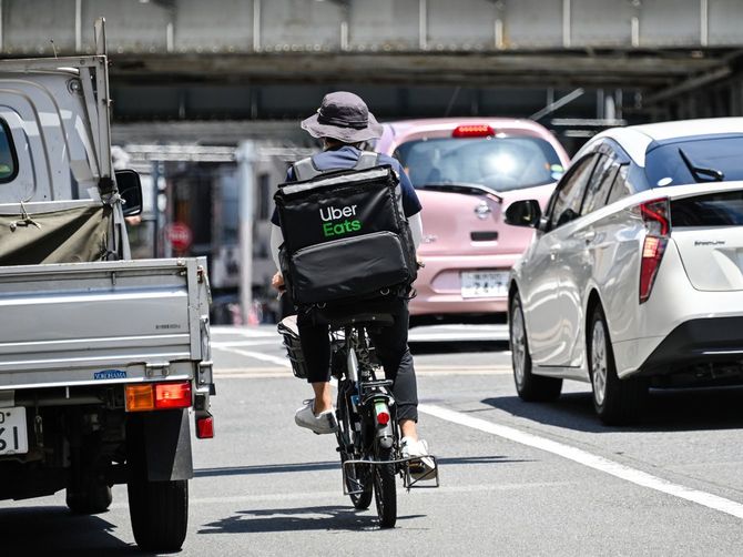 ブレーキランプが点灯している車の間をすり抜けて走るUber Eatsの配達員