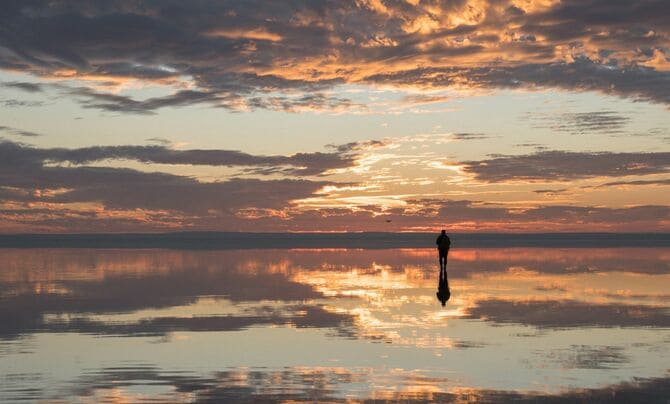 夕暮れの塩湖に立つ男性