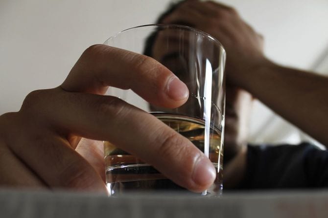 すでにだいぶ飲んでいる男性がグラスに手をかけ、片方の手でおでこを支えている