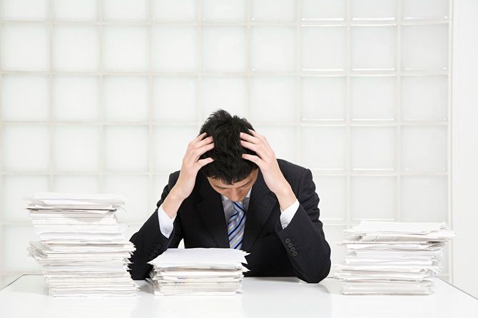 うず高く積まれた書類に囲まれストレスを抱えている男性