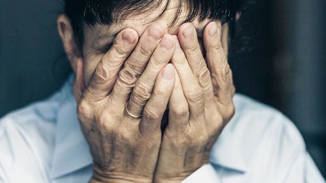 悲しむ高齢女性が手で顔を覆う