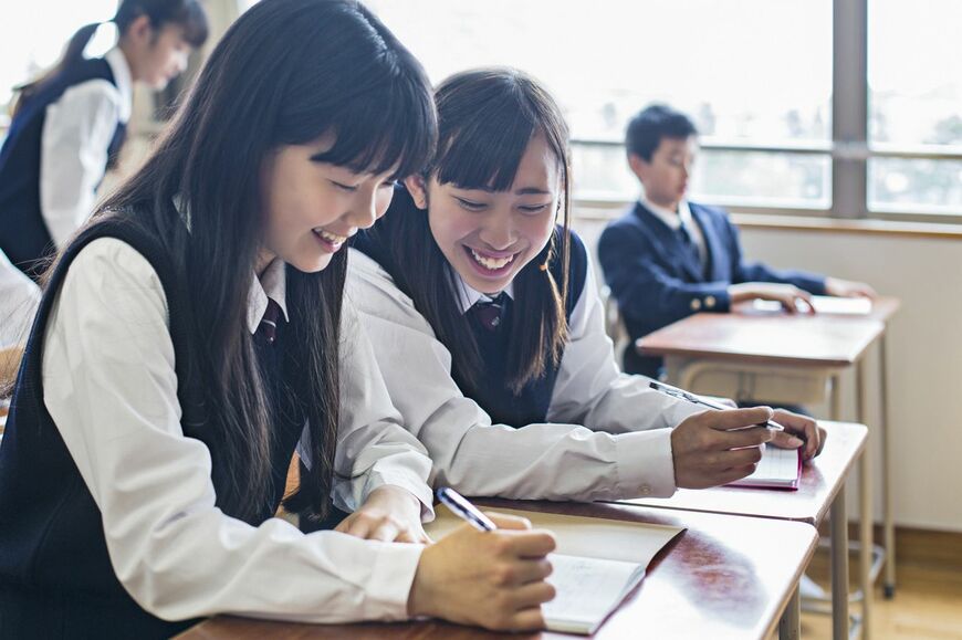 教室でノートに書き込んだもので笑顔になっている二人の女性生徒