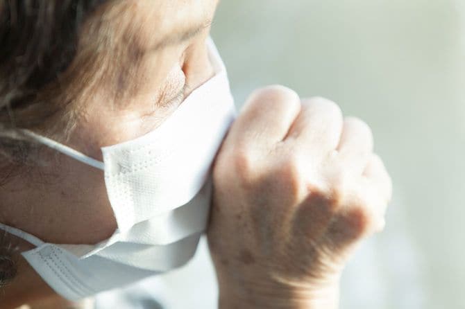 不織布マスクを着用したシニア女性がせきをしている