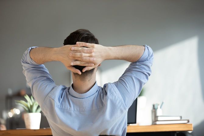 労働者が机に座り、手を頭の後ろに回している