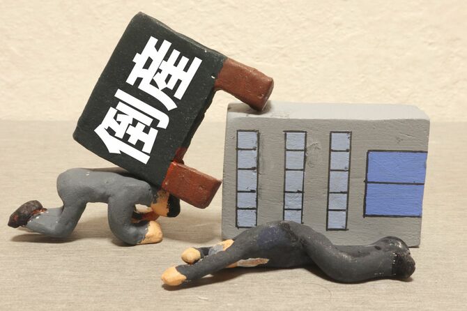 倒れたビルと「倒産」の文字の看板、倒れるサラリーマンの人形