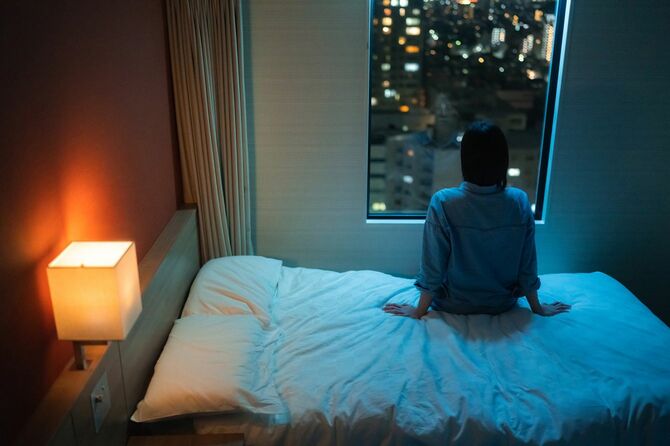 ホテルのベッドに腰かけ、外を見つめる女性