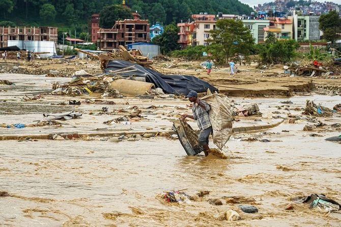 ネパールの洪水被災地で、土砂や瓦礫が散乱する中、荷物を持って歩く男性