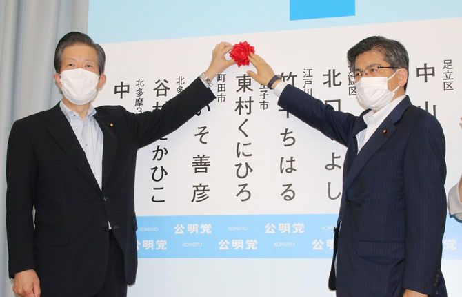 東京都議選で当選確実の候補者の名前に花を付ける公明党の山口那津男代表（左）と石井啓一幹事長＝2021年7月4日夜、東京都新宿区の公明会館
