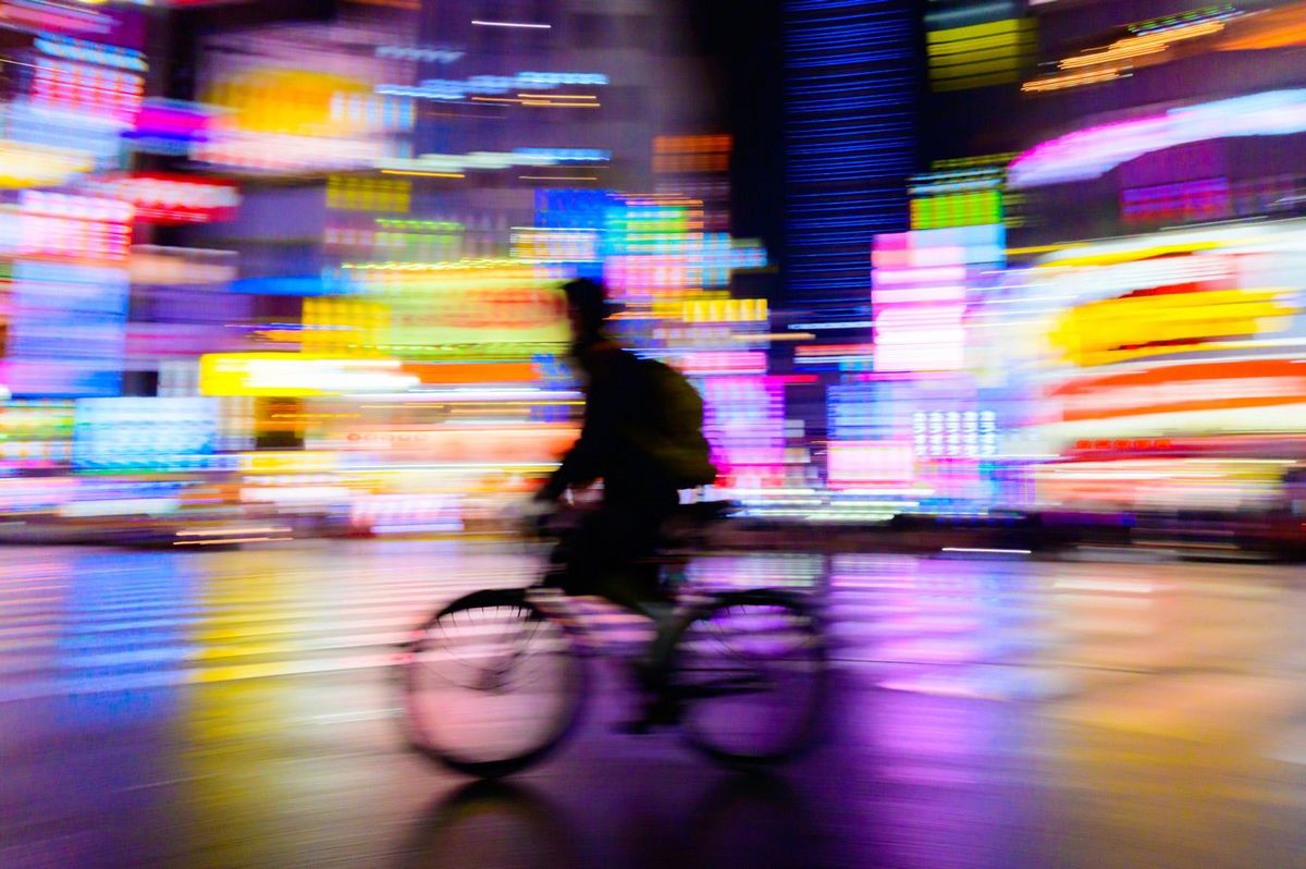 夜の新宿、ネオンが光る街を自転車で通り過ぎる男性