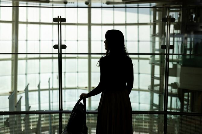 空港で、スーツケースにバッグを載せて持つ女性