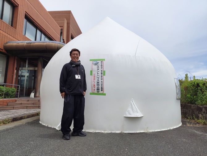 八代市役所の鏡支所の一角に建てた見学用のインスタントハウスの前に立つ、名古屋工業大学教授の北川啓介さん