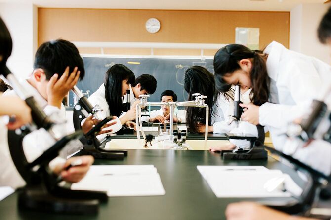 全員で顕微鏡をのぞきながら理科の授業を受ける生徒たち