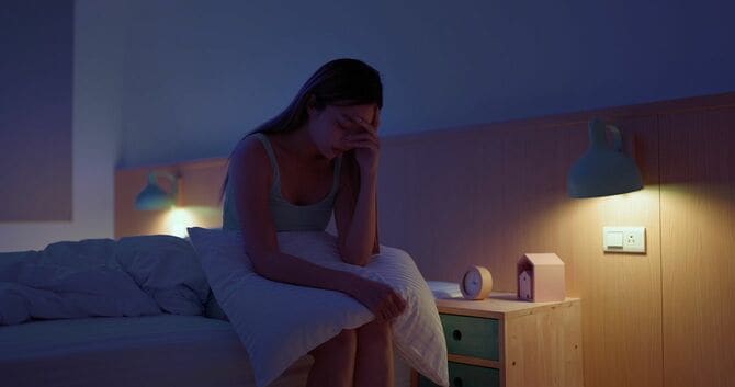 ベッドの縁に腰かけて額を押さえる女性
