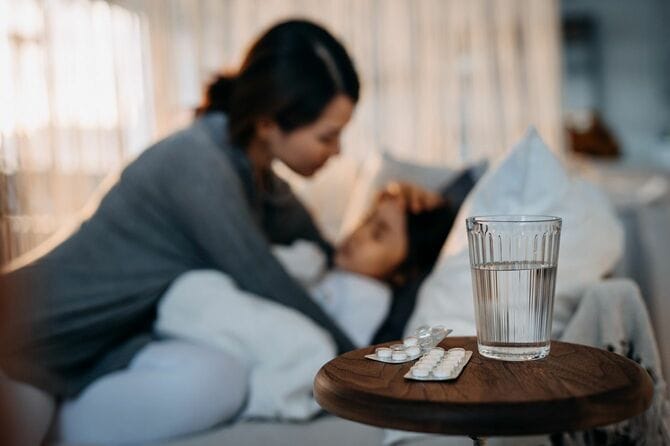 娘を看病する母親とベッドサイドの錠剤と水の入ったコップ