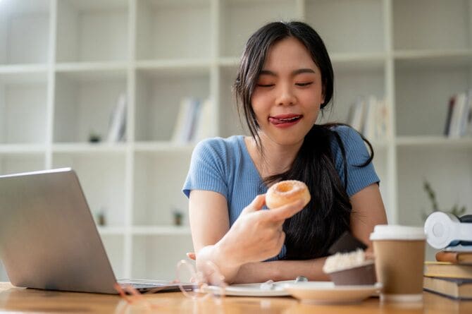 自宅の勉強机でドーナツを食べながら、おやつの時間を楽しんでいる女性